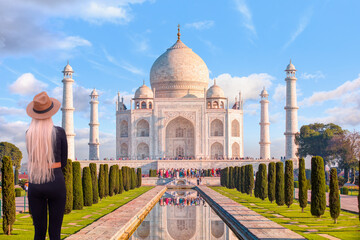 A blonde woman wearing black tights and a beige hat is standing - Taj mahal front view with...