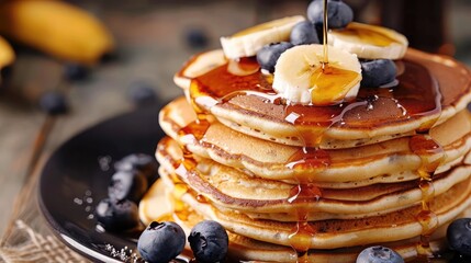 Delicious banana pancakes stacked high on a plate, drizzled with maple syrup and garnished with banana slices and blueberries. - Powered by Adobe