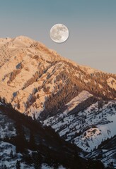 The moon is behind the top of a snow-covered mountain. Night sky with stars.