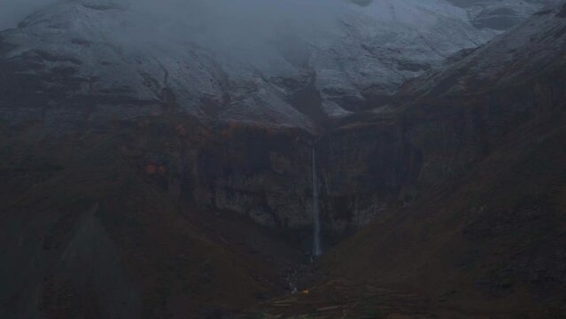 Slow motion shot of Sissu waterfall with snow on top of it after snowfall during the winter storm at Sissu in Lahaul and Spiti district, Himachal Pradesh, India. Waterfall under snowy mountain peaks.