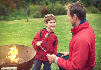 Father, outdoors and son with marshmallow for roasting on flame with bonding for happiness. Child development, smile and camping with scenic campsite in winter morning on weekend away to Germany.