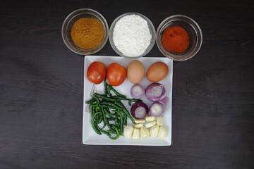 Eggs, tomatoes, green chilies, garlic, onions, spices, chives, chili powder and corn flour are arranged on the table