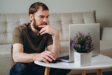 A man works on a laptop in a room at a coffee table