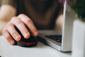 A male hand holds a computer mouse near a laptop.