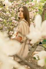 A beautiful woman sits on a magnolia branch among blooming buds.