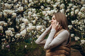 A young woman is talking on the phone against the background of a white magnolia tree.