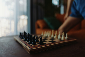 The strategic game of chess being played by a person in front of a window on a table