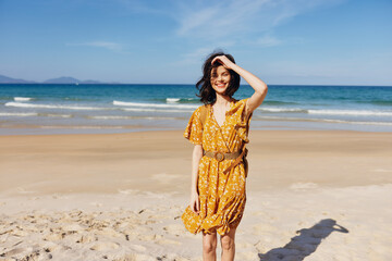 Woman in yellow dress standing on beach with hands on head reflecting on the beauty of nature