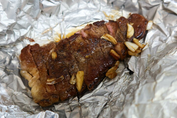 close up of homemade baked roasted sliced beef steak with fried garlic on aluminium foil