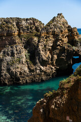 Ponta da Piedade near Lagos in Algarve, Portugal. Cliff rocks and tourist boat on sea. Praia Dona Ana, Estudantes beach. Sunny day. Point of Pity