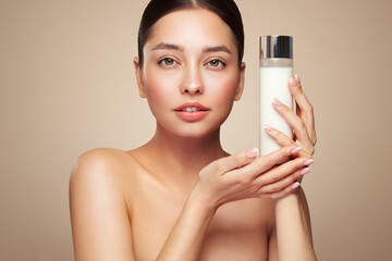 Smiling woman holds bottle with cosmetic milk. Photo of attractive woman with perfect makeup on...