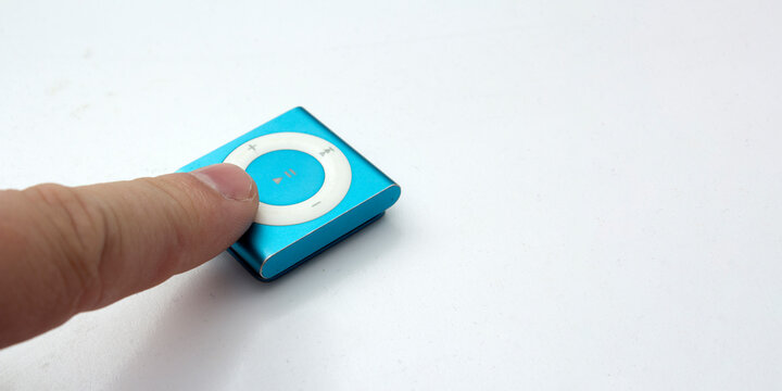 Saint-Petersburg, Russia - May 10, 2022: Male finger pokes at old blue small metal square music player iPod Shuffle on white background. Concept of vintage, technique, technology, mp3, sing, song