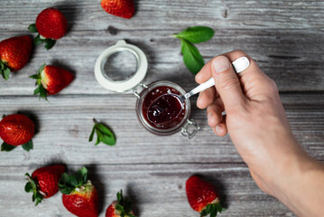 Man holding a teaspoon with strawberry jam. Delicious homemade strawberry jam, healthy breakfast.