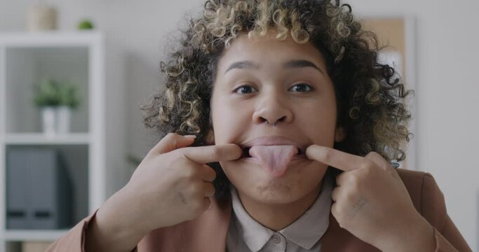 Loop portrait of joyful African American businesswoman making funny grimace showing tongue looking at camera in office. Face expression and businessperson concept.