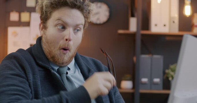 Loop of male employee taking off and putting on eyeglasses looking at computer monitor in office in evening. Modern technology and eyewear concept.