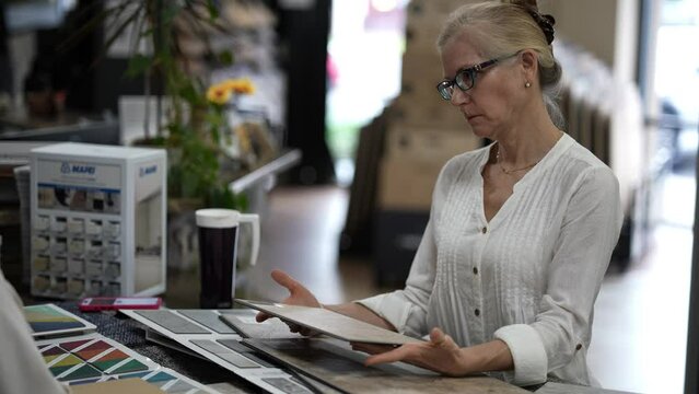 Happy mature woman talking to sales associate about floor tiles in a store, consider using vct, lvp or engineered tile in a home renovation project.