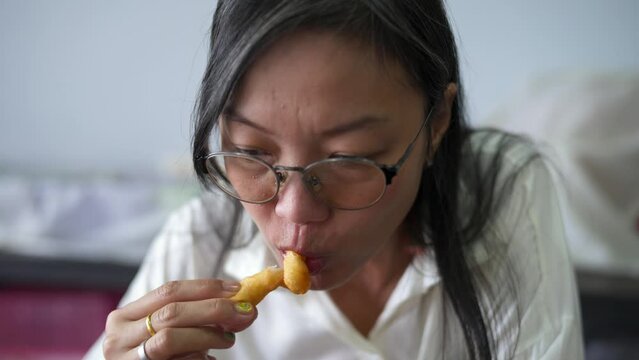 An Asian woman took a patongko and dipped it in a hot Thai tea cup and ate it deliciously