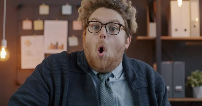 Loop portrait of funny businessman making surprised face looking at camera with astonishment in office in evening. Business and emotion concept.