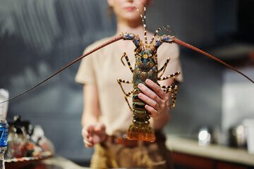 Woman holding lobster in hand standing in front of counter in seafood market