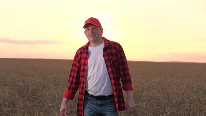 Happy modern male farmer going at sunset autumn dry wheat field closeup. Proud man smiling walking...