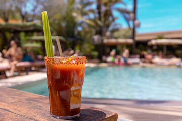 Close up shot of a Bloody Mary cocktail with a celery stick inside and crushed spices on the glass' edge at the pool, in a sunny afternoon in Ibiza. Vacation mood, relax, pool party vibes.