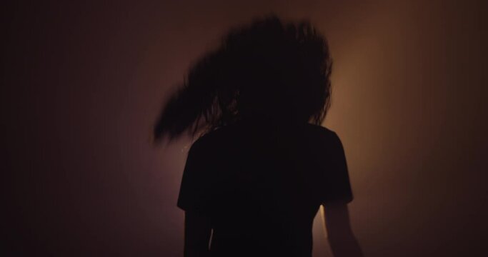 Silhouette of a person with long hair head banging 