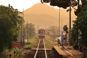 夕陽が眩しいローカル線のプラットホームと踏切のある風景