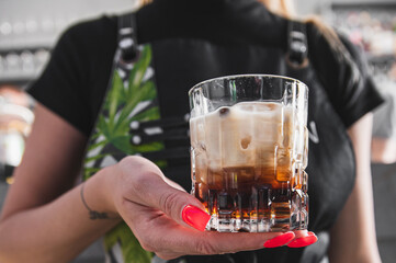 A person holds a glass of iced cocktail, with a blurred background