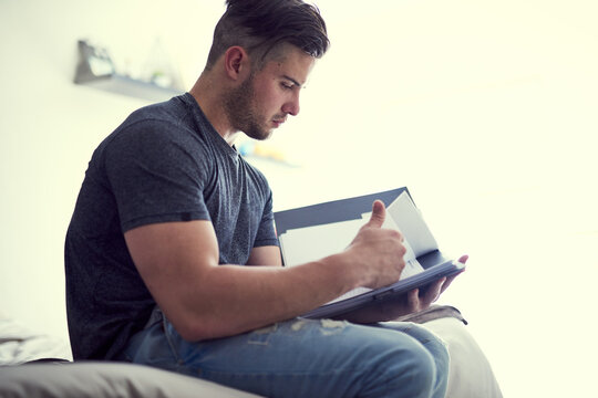Document, man and student in home with studying for test or exam, weekend revision and learning for knowledge. Bedroom, male person and reading paperwork for assessment with education and scholarship