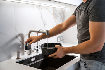 A man pours water from a tap into a pot in the kitchen