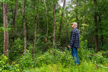 Senior man with binoculars in the trees of a dense forest in southeastern Texas.