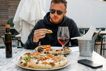 Young fashion fun guy eating pizza with glass of vine. Sunglasses, a great carefree day, urban style