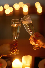 Champagne, toast and hands of couple for celebration with candle light, happy relationship and date...