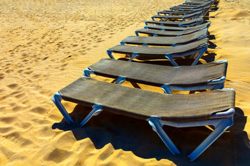 Sun loungers in a row on the sandy beach. Beach chairs stretches across the sandy shore. Place for...