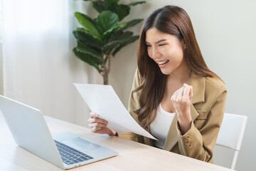 Happy cheerful asian young woman holding paperwork, reading tax refund paper bill, receive good...