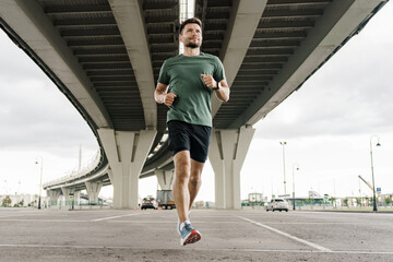 A man runs under a large bridge, showing determination and focus in his athletic stride.