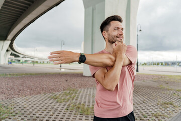 A man stretches his arm under a bridge, preparing for an outdoor workout session with determination.