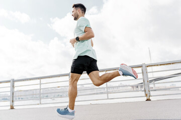 A man runs on a waterfront path, demonstrating athleticism and speed, with a city bridge in the background.