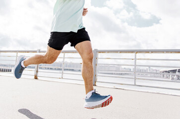 A man in a mint green shirt and black shorts runs by the waterfront, focusing on his running shoes.