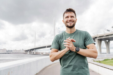 Man stretching his arm, wearing a green shirt, by a bridge.