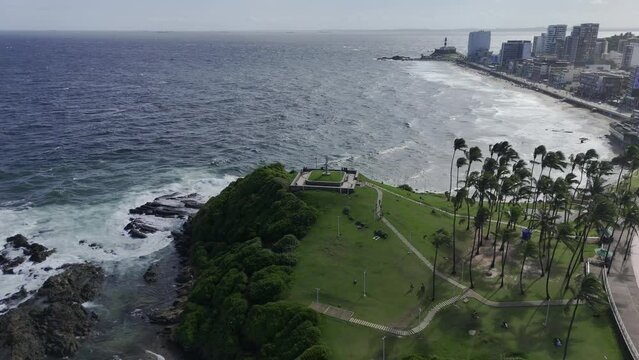Drone descends on Morro do Cristo with Farol da Barra in the distance in Salvador, Bahia, Brazil