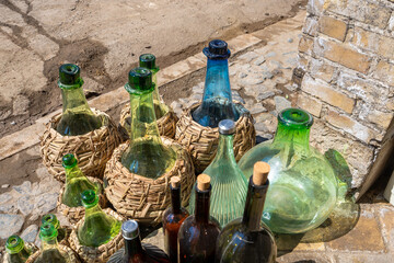 A variety of glass bottles, some in woven baskets, are displayed outside the store. Sunlight...