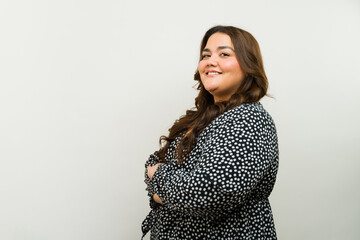 Happy plus-size woman in a dress smiling and posing with arms crossed against a neutral background