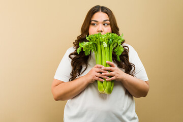 Latin plus-size woman playfully posing with a bunch of fresh celery in a studio setting
