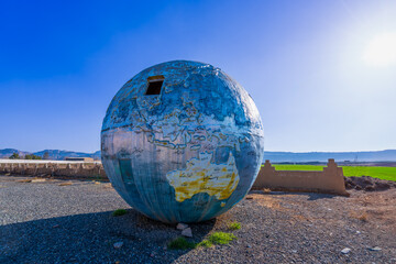A dilapidated globe monument stands under the blue sky, hinting at its past glory in its...