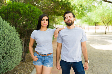 Confident young hispanic couple in grey t-shirts posing in a lush park for branding mockups