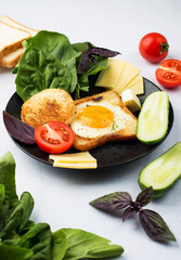 Toast with egg, cheese, cherry tomatoes, cucumbers, spinach, basil on a plate on a light background. European breakfast. Top view, horizontal.