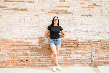 Full length view of a latin woman in black t-shirt and denim shorts, posing with sunglasses against...