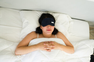 Peaceful woman wearing an eye mask sleeps soundly in a bright bedroom, lying comfortably in a clean...