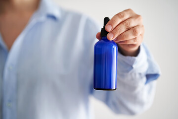 Female hands in a blue shirt hold a blue bottle of serum.